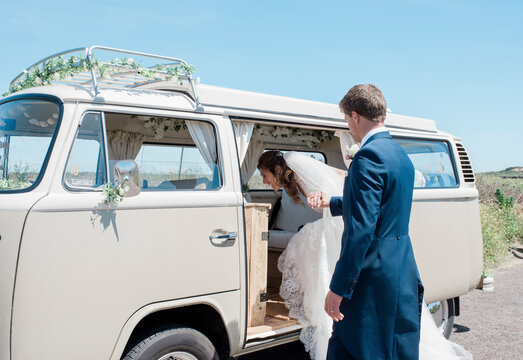 groom helping bride get into a camper van on their wedding day