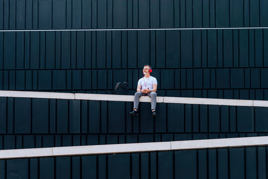 Mature man sitting on a wall listening to music with headphones