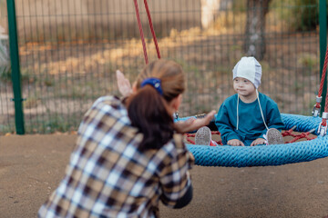 Cute Little boy with down syndrome in a funny hat with his mother, swinging on a swing, soap bubbles