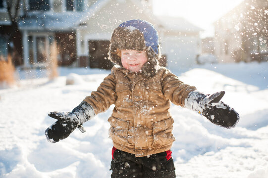 Toddler boy playing and smiling while throwing snow in front of house