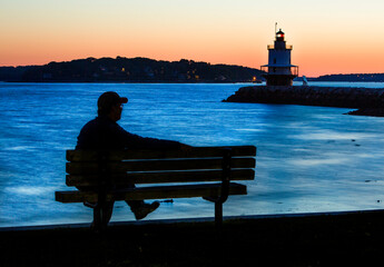 Silhouetted man watches pre-dawn glow near coast of Maine lighthouse