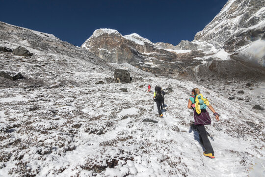 Women climbers ascend a snowy hill below an imposing rock wall
