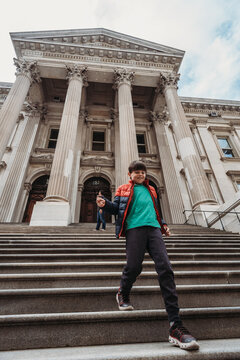 Young Boy Running Down Steps Of A Big Stone Building In New York City.