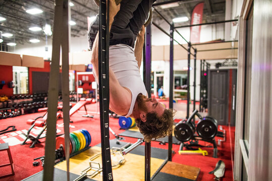 Fit man hangs upside down on gymnastic rings at the gym