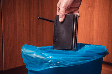 A man throws a WiFi router in the trash. Man's hand with a WiFi router and a trash can in blue