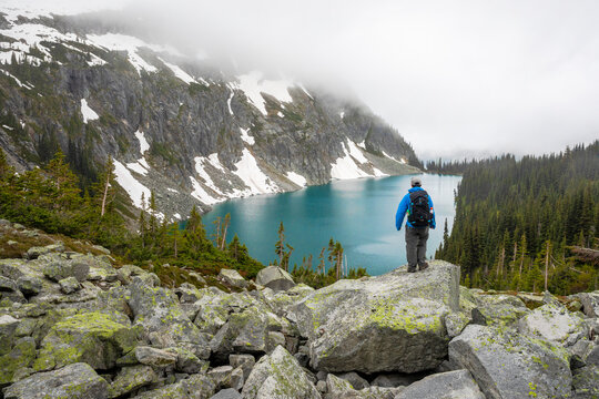 A man takes in the view of a beautiful alpine lake on a cloudy, rainy summer day in the Coast Mountains around Pemberton, British Columbia.