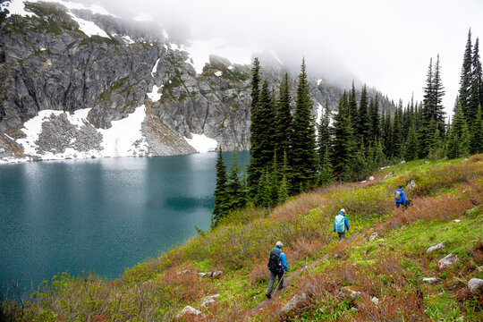 A group of people hike around a beautiful alpine lake on a cloudy, rainy summer day in the Coast Mountains around Pemberton, British Columbia.