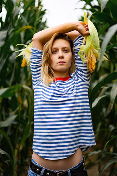 Young woman in stripped ves shirt in a corn field picking up the corn.