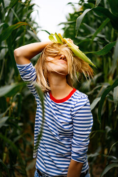 Young woman in stripped ves shirt in a corn field picking up the corn.