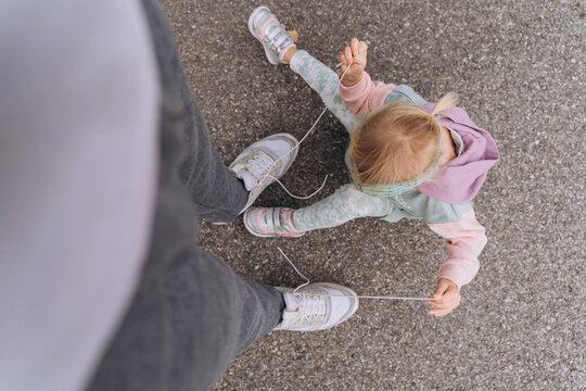 stylish baby girl in a hoodie hooligan unties dad's shoelaces