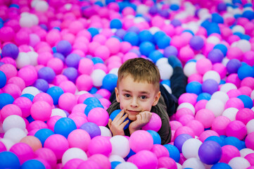 Fototapeta na wymiar A beautiful little smiling boy, a preschool child lies in multi-colored plastic balls on the playground. Photography, childhood vacation concept.