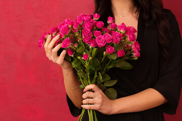 A woman in a black dressing gown holds a bouquet of pink roses, on a pink background, close-up