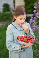 Cute little girl in a vintage dress eats strawberries in the garden