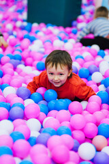 Obraz na płótnie Canvas A beautiful little smiling boy, a preschool child lies in multi-colored plastic balls on the playground. Photography, portrait, childhood vacation concept.