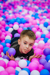 Fototapeta na wymiar A beautiful, happy, small, smiling boy, a preschool child lies in a pile of multi-colored, colored plastic balls on the playground. Photography, portrait, concept.