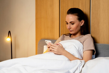 Young woman lying in bed and using a smartphone late at night cannot sleep. The concept of sleep disorder. Dependence on a mobile phone