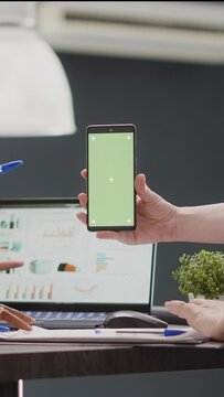Vertical video: Diverse group of employees working with greenscreen on smartphone, using isolated display with chroma key. Startup workers checking mockup template in business coworking space