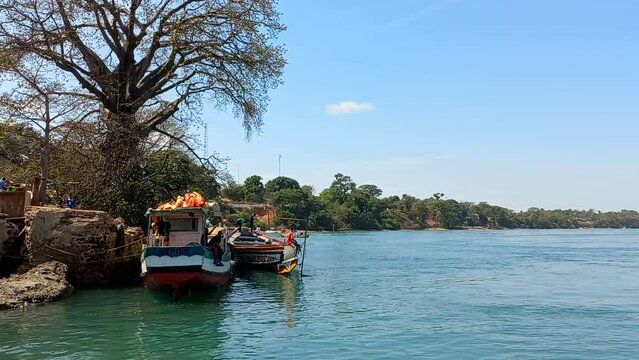 Port of Bubaque on the Bijag&oacute;s island, with two small colorful transport boats and many trees in the background.