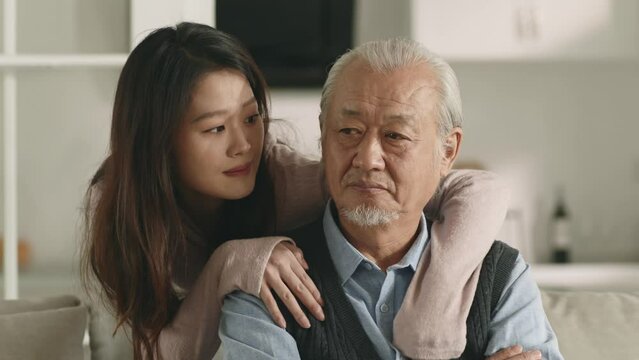 young asian adult daughter consoling sad and unhappy senior father at home