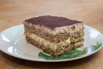 Tasty homemade tiramisu close-up on white plate with green leaf decoration, on rustic ceramic counter. Healthy dessert with creamy cocoa, coffee layers