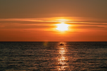 Obraz premium Small fishermen boat with scenic sunset view from Sveti Stefan at Adriatic Mediterranean Sea, Budva Riviera, Montenegro, Europe. Reflection of sun beams on water surface. Summer vacation atmosphere