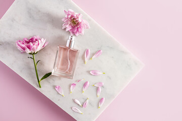 a bottle with a cosmetic product or perfume lies on a marble white podium with petals and flowers of a lilac . a copy space. product presentation.
