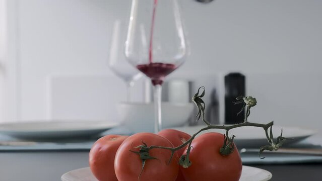 Vino tinto de primera calidad servido con precisi&oacute;n en una cocina moderna con tomates en rama en primer plano