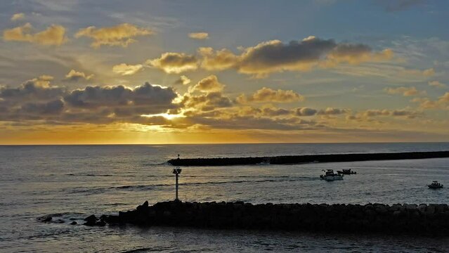 Drone shot of a Southern California Sunset near jetty with boats coming and going in the Oceanside harbor.