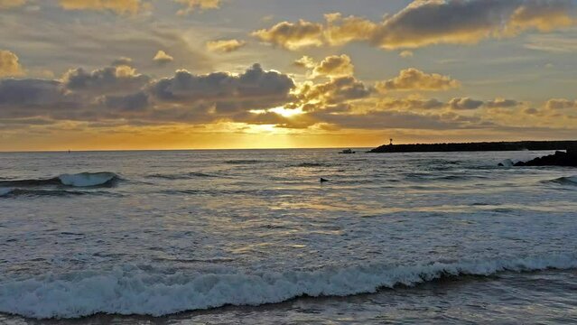 Paning shot of surfer waiting for waves during a beautiful Southern California Sunset at the Oceanside Jetty.