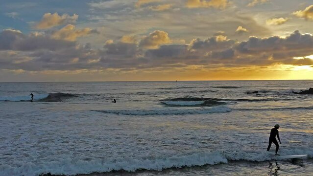 Panning Drone Shot of surfers surfing during a beautiful Southern California Sunset at the Oceanside Jetty.