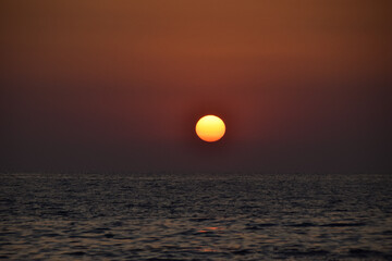 Vibrant sunset descending on the horizon, sea in golden colors, small waves gently touching the sands,