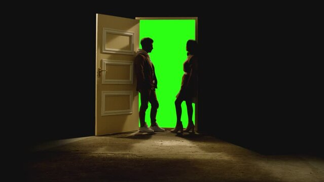 Side view of couple standing opposite and looking each other in front of an open door with darkness behind . Footage of couple stand on floor near door with green screen .  Concept of dream or romance