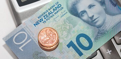 New Zealand cash - ten dollar note with small change over a calculator in web banner format.