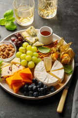 Cheese plate with various cheeses, fruits, nuts and snacks. Dark background.
