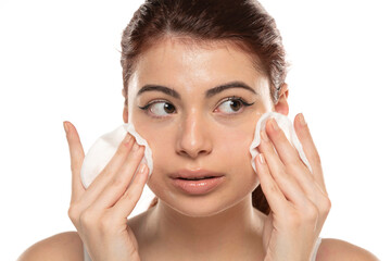 Beautiful redhead woman cleaning her face with cotton swab over white background