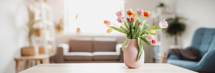 A bunch of tulips in pink vase standing on the wooden table indoors. - obrazy, fototapety, plakaty