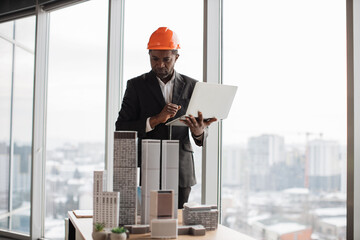 Confident afro-american man in suit using laptop looking at the architecture design of buildings at...