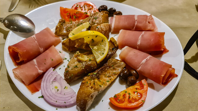 Typical Montenegrin appetizer served in local restaurant in Virpazar, Bar, Montenegro, Balkans, Europe. Platter with ham (prosciutto), grilled fish, onions, tomatoes and lemon.