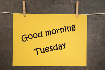 Napis Good morning Tuesday na wiszącej żółtej kartce na ciemnym tle - obrazy, fototapety, plakaty