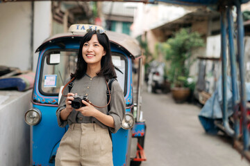 Naklejka premium Young Asian woman backpack traveler standing a side of Tuk Tuk taxi on summer vacations at Bangkok, Thailand.
