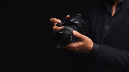 Photographer in a suit holding the digital camera while standing on a black background