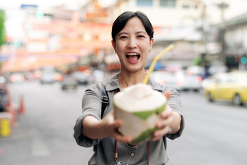 Happy young Asian woman backpack traveler drinking a coconut juice at China town street food market...