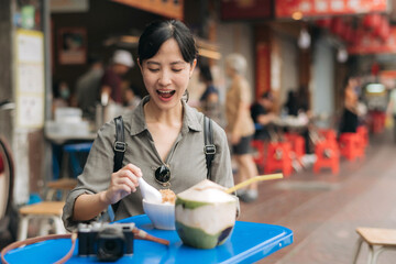 Happy young Asian woman backpack traveler enjoying street food at China town street food market in Bangkok, Thailand. Traveler checking out side streets.