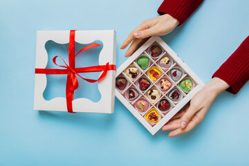 Female hands with delicious candies in box on color background