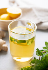 A glass of tea with fresh lemon, mint and ginger on a light background with morning light close up.