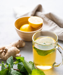 Aroma glass of tea with fresh lemon, mint and ginger on a light background with morning light.