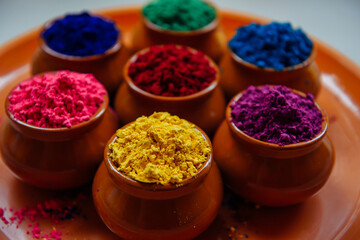 Obraz na płótnie Canvas Colorful Holi powder in cups on a tray closeup. Bright colours for Indian holi festival in clay pots. Selective focus