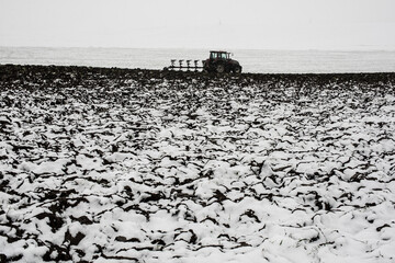 Late ploughing at the end of November in heavy snowfall. Tractor plowing. - 571877997