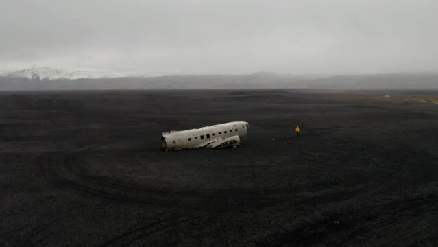 Aerial: Slow panning shot of one person standing in front of DC3 plane wreck in Iceland