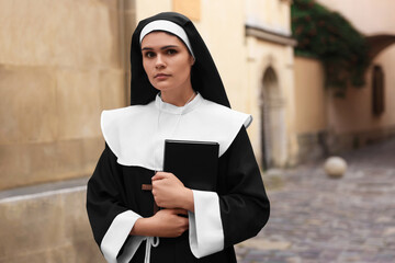 Young nun with Christian cross and Bible near building outdoors